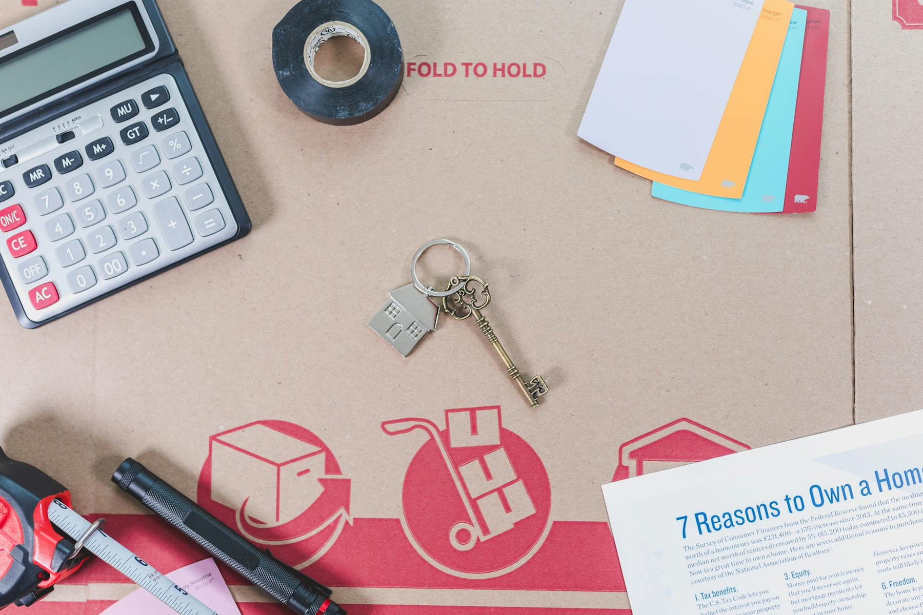 Flat lay of home buying essentials with calculator, keys, tape, and color swatches. on The Smart Home Buyer