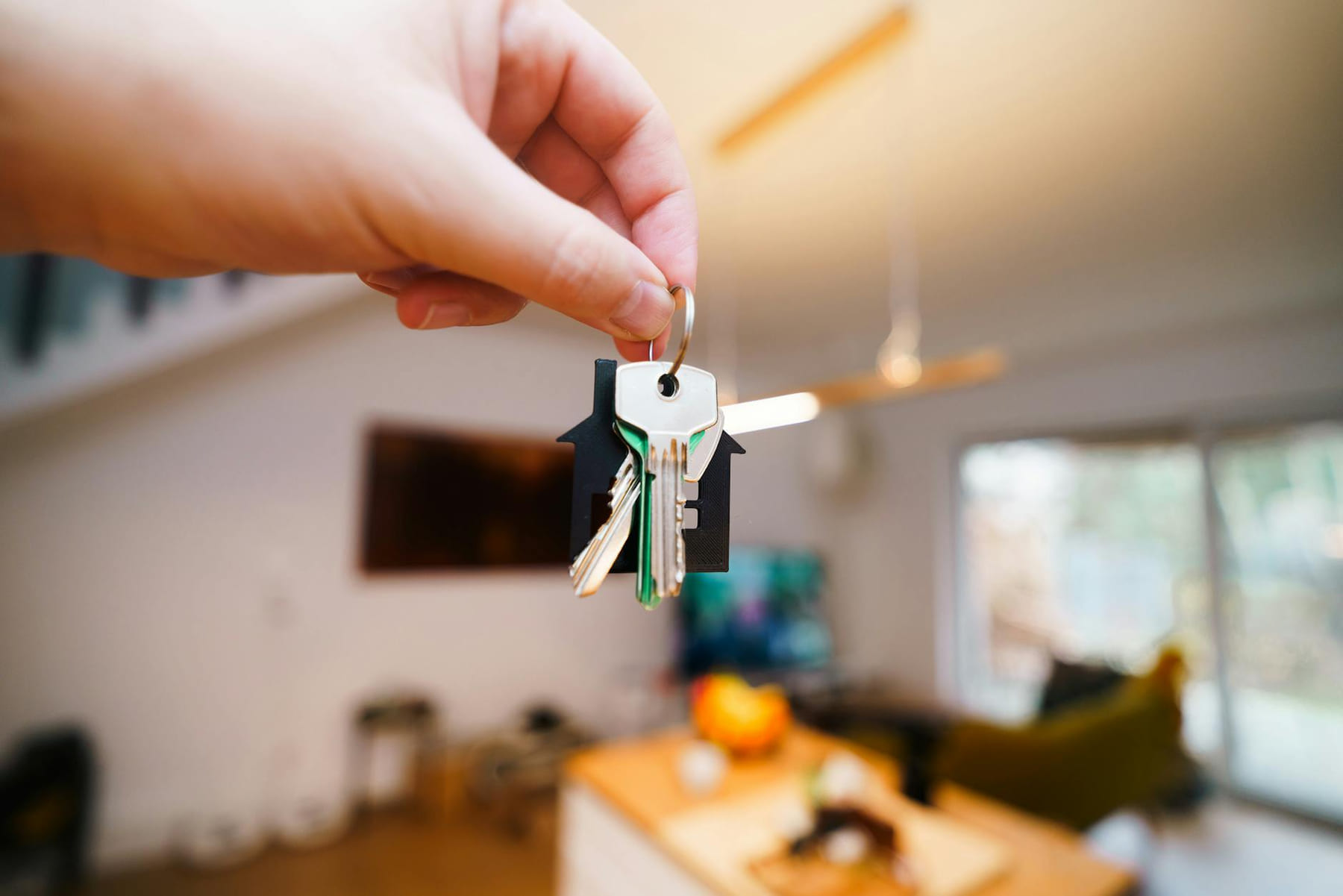 A hand holds keys with a house keychain inside a modern, well-lit living space. on The Smart Home Buyer