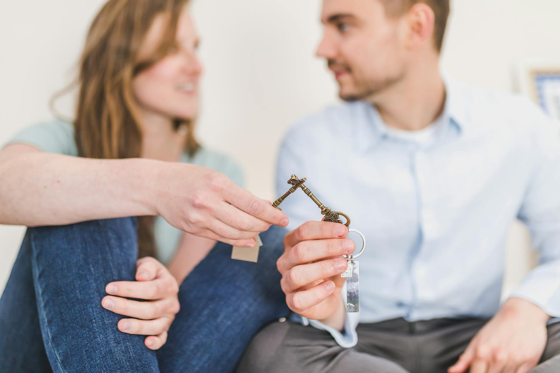 A young couple sitting together exchanging keys, symbolizing new home ownership on The Smart Home Buyer