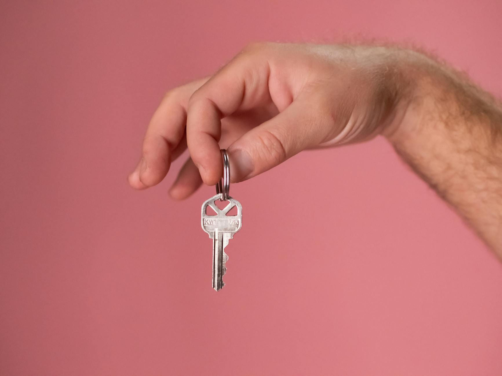 Hand holding a silver key with a pink background, symbolizing new home ownership. on The Smart Home Buyer